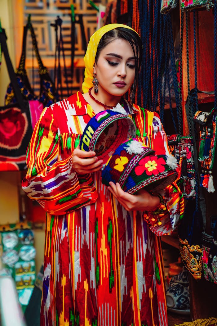 Woman in colorful traditional clothing browsing vibrant handmade hats in a market.